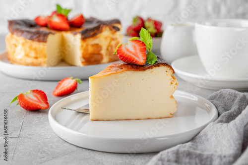 A piece of Basque burnt cheesecake or San Sebastian cheesecake with fresh strawberries on a white plate on a gray background. Selective focus. Copy space.