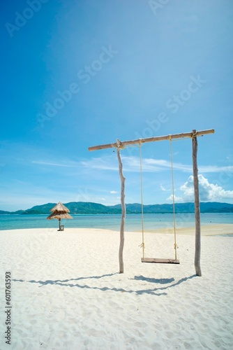Wooden swing on a beach with clear blue sky on sunny day.