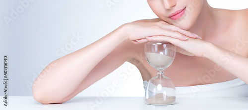Closeup personable model holding hourglass in beauty concept of anti-aging skincare treatment. Young girl portrait with perfect smooth clean skin and flawless soft makeup in isolated background