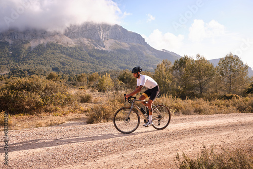 Cyclist practicing on gravel road.Fit male cyclist riding a gravel bike on a gravel road with a view of the mountains, Alicante region of Spain