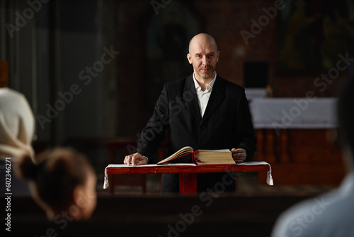 Mature pastor reading Bible for believers while standing at altar in church