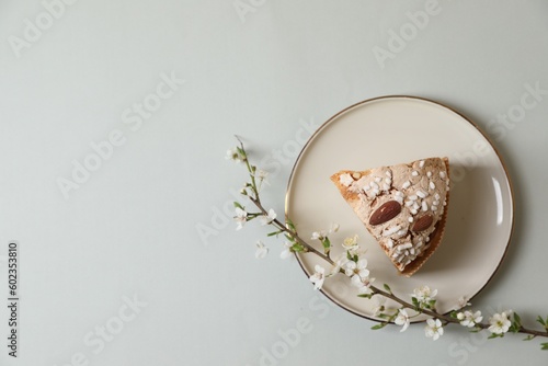 Plate with piece of delicious Italian Easter dove cake (traditional Colomba di Pasqua) and flowering branches on light grey table, top view. Space for text