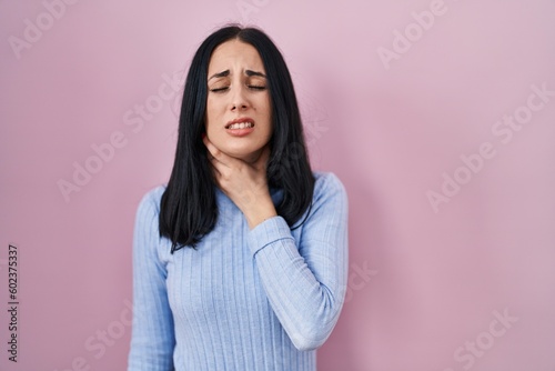 Hispanic woman standing over pink background touching painful neck, sore throat for flu, clod and infection