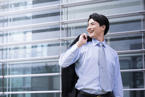 中途採用や転職のイメージに オフィスビルの前で振り返る笑顔の黒髪30代男性社員 コピースペース