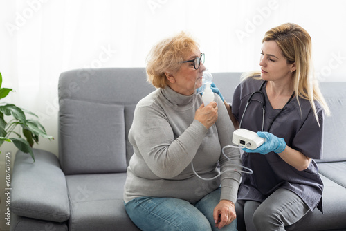 Young girl doctor makes inhalation to an older woman on a white background. Fight nasal congestion and rhinitis.