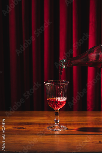 Lambrusco bottle pouring into glass, background of red velvet curtains and wooden table 