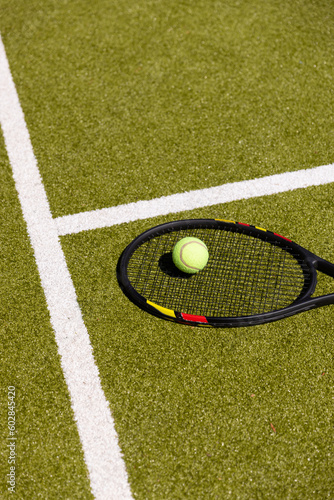 Tennis ball on tennis racket lying on sunny outdoor grass tennis court, with copy space