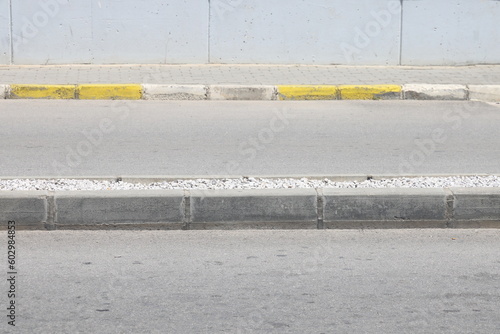 A street border painted in white and black on the background of the road and green foliage in the summer closeup. Road safety, minimalism.