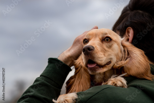 A man holds a cocker spaniel puppy in his arms and strokes his head. A brunette man stands on the street hugging his dog.
