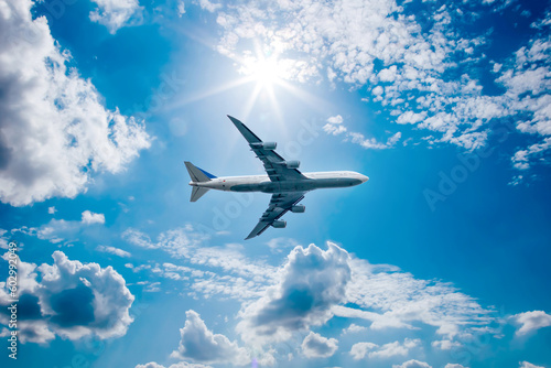 Airplane in the blue sky with clouds from below, high flying passenger plane. jet plane flying overhead diagonally in sky with sunlight. Bottom view