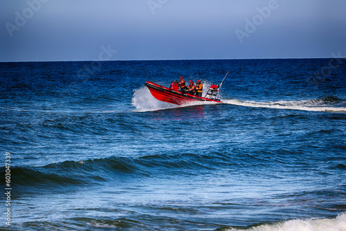Pomarańczowa łódka z ratownikami płynie z akcją ratowniczą na morzu. 