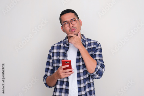 Adult Asian man holding mobile phone with suspicious expression