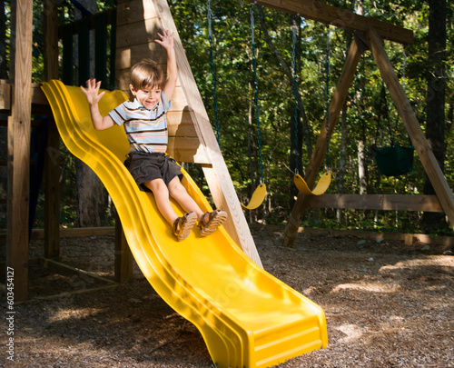 Hispanic boy sliding down outdoor slide with arms raised above head.