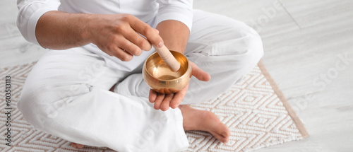 Young man with Tibetan singing bowl meditating at home, closeup