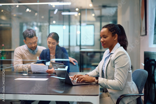 Black female insurance agent works on laptop during meeting with clients in office.