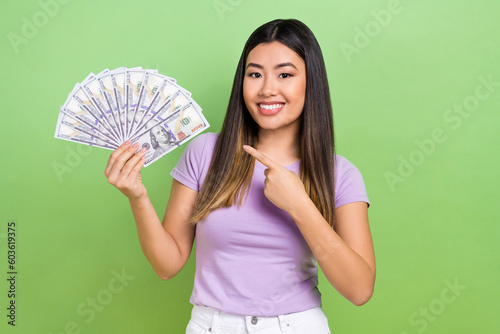 Photo of young chinese woman brown hair wear violet t-shirt point finger first high income banknotes isolated on green color background