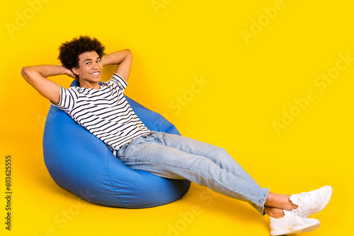 Full body photo of young student chilling dormitory hands head take nap after lectures sitting pouf isolated on yellow color background