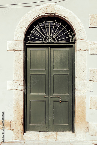 Green wooden front door with transom window in natural stone arched doorway in sunlight
