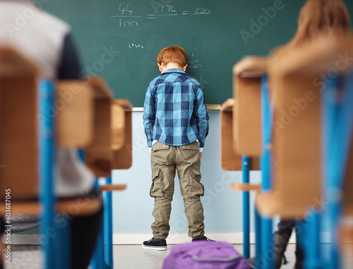 Rear view, boy student in detention with head on chalkboard and in classroom of school building. Anxiety or depressed for time out, math problems to solve and male kid with back to class.