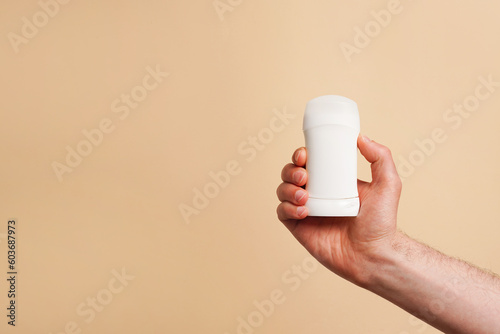 Male hand holding white deodorant on beige background. Closeup. copy space