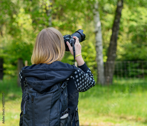 Kobieta w blond włosach z plecakiem na plecach fototrafująca obiekt w lesie, lato i fotografka