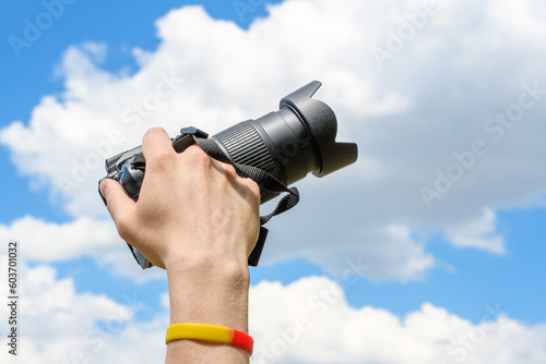 Dłoń trzymająca aparat fotograficzny na niebieskim tle chmur na niebie 