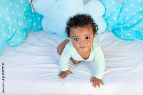 cute african baby sitting in bed at home before going to bed on a blue bed and looking up, the concept of healthy sleep and baby bedding cotton accessories