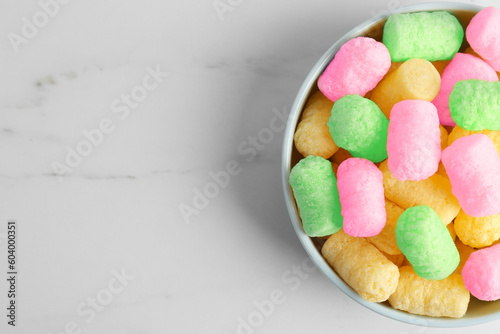 Bowl with colorful corn puffs on white marble table, top view. Space for text
