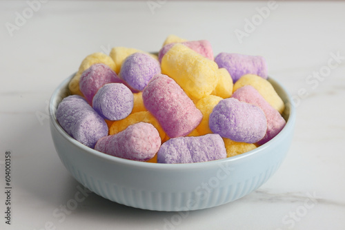 Bowl with colorful corn puffs on white marble table, closeup