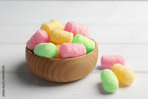 Bowl with colorful corn puffs on white wooden table, closeup