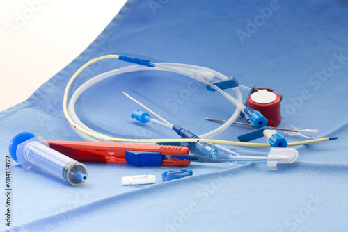 Kit for placement of central venous catheter with red scalpel, blue syringe, guide wire, introducer needle, vessel dilator, and injection caps on blue surgical drape in operation theatre