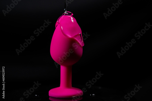 Pink anal plug in intimate lubricant on a black background. 