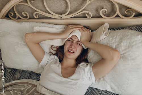 Young woman with headache flu ill sick disease cold at home indoor lying on bed with cold compress on her head at bedroom home