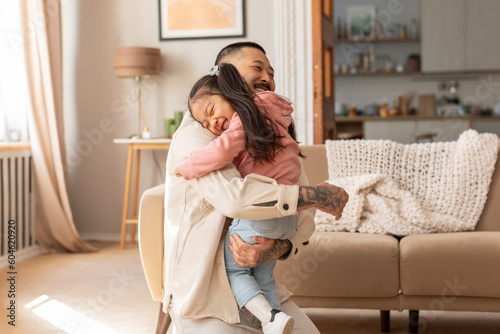 Loving Asian Dad Embracing Little Baby Daughter In Living Room