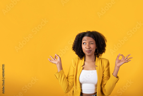 Funny curiously black lady looking with one eye at free space, meditating isolated on yellow background, studio shot