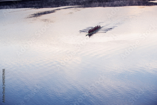 Rowing crew rowing scull on lake in distance