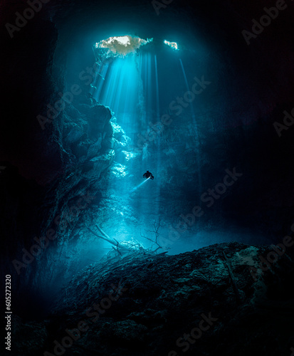 Person swimming in an underwater cave illuminated by a bright light in Tulum, Mexico.
