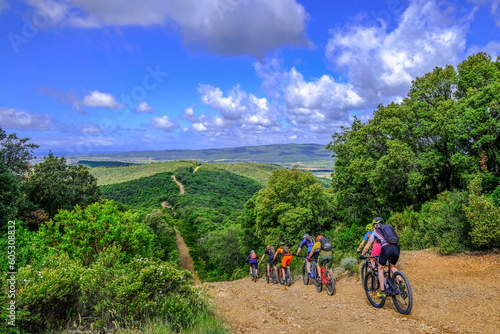 Unrecognisable mountain bikers ride on a firebreak trail over the beautiful landscape with its hills in Tuscany, Massa Marittima, Italy