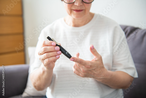 Cropped image older woman using glucose meter alone at home. Unhealthy middle aged retired lady testing blood sugar ranges in morning, putting lancet pen on finger. Diabetes, healthcare concept