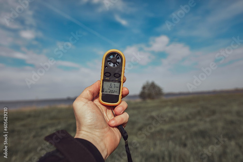 Person holding modern digital anemometer outdoors for measuring wind speed, temperature, humidity and other atmospheric effects.