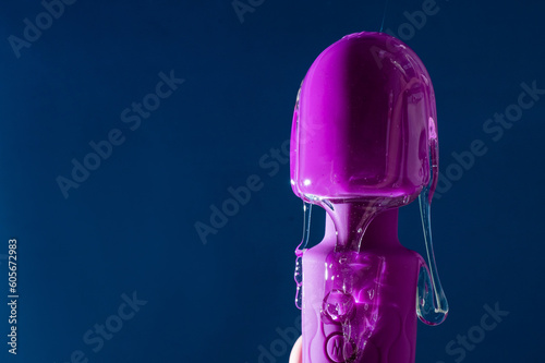 Intimate lubricant pours on a purple vibrator on a blue background. Copy space. 