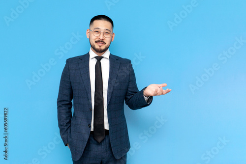 asian businessman in suit and glasses shows his hands to the side, korean entrepreneur advertises copy space