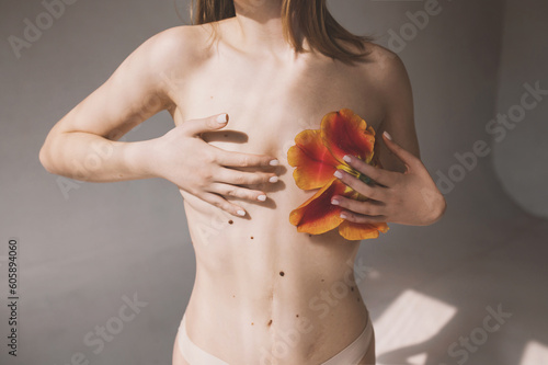 Girl in underwear with red tulip close breasts. Breast cancer awareness concept. Naked young woman covers breasts with hands. Topless female with breast covered with flowers cropped image 
