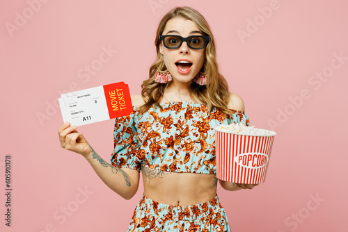 Young fun exultant excited fun woman in 3d glasses wear summer casual clothes watch movie film hold ticket bucket of popcorn in cinema isolated on plain pastel light pink background studio portrait.