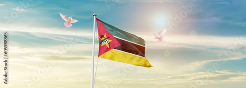 Waving Flag of Mozambique in Blue Sky. The symbol of the state on wavy cotton fabric.