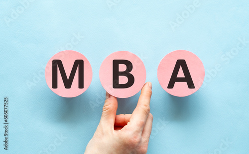 Hand writing MBA - with Hand on pink paper, blue background