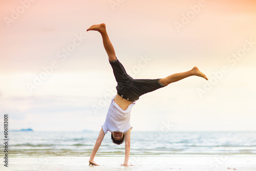 Teenager doing calisthenics exercise. Beach yoga.