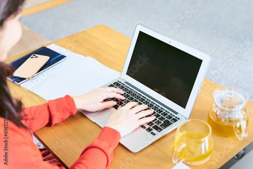 リビングのローテーブルにパソコンを広げキーボードでタイピングをして入力作業をする30代女性の手元