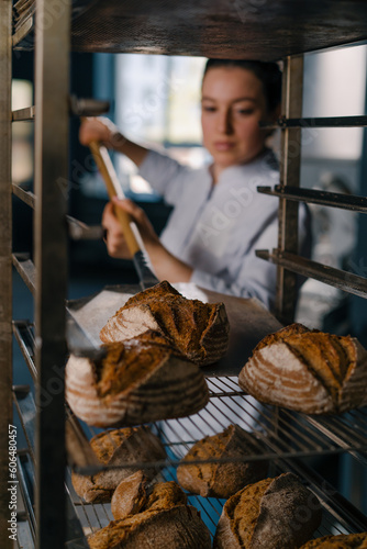 female baker takes out freshly baked fresh bread from the oven and puts it on the shelf in the kitchen of the bakery Culinary profession
