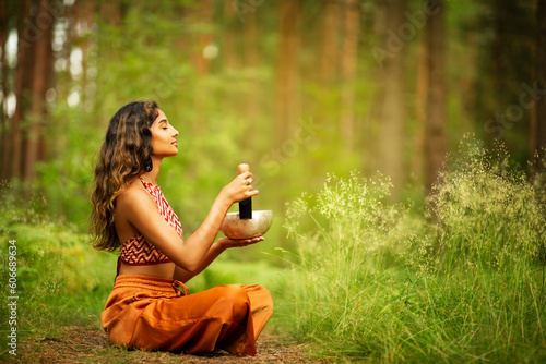 Indian Woman playing Tibetan Singing Bowls with Mallet Outdoors. Relaxing Meditative Music Therapy and Sound Healing. Spiritual Yoga Meditation Practice in Forest